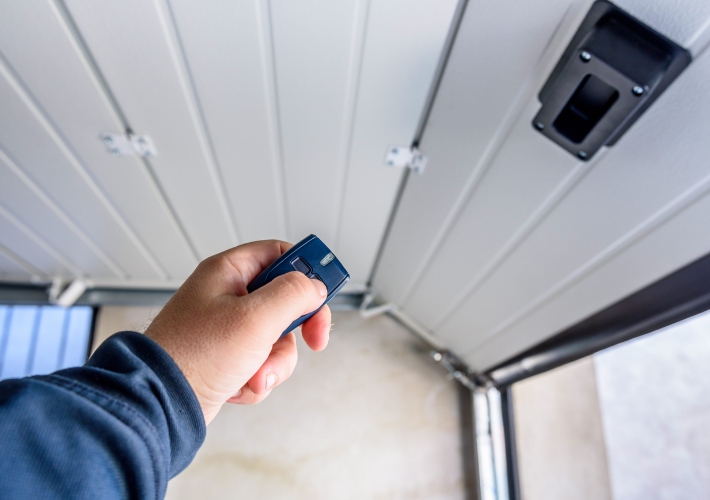 Person using remote control to open garage door in residential area on a sunny day garage door opener installation service