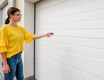 Woman in yellow shirt uses remote control to open a white garage door in a modern residential setting Smart home integration with your garage door opener system
